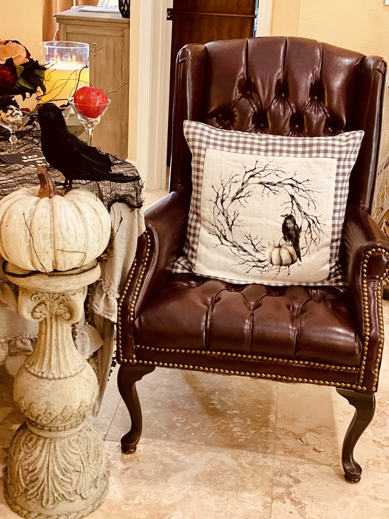 Halloween decor pumpkin on top of candlestick with crow on top tree branch matching pillow cover on leather chair